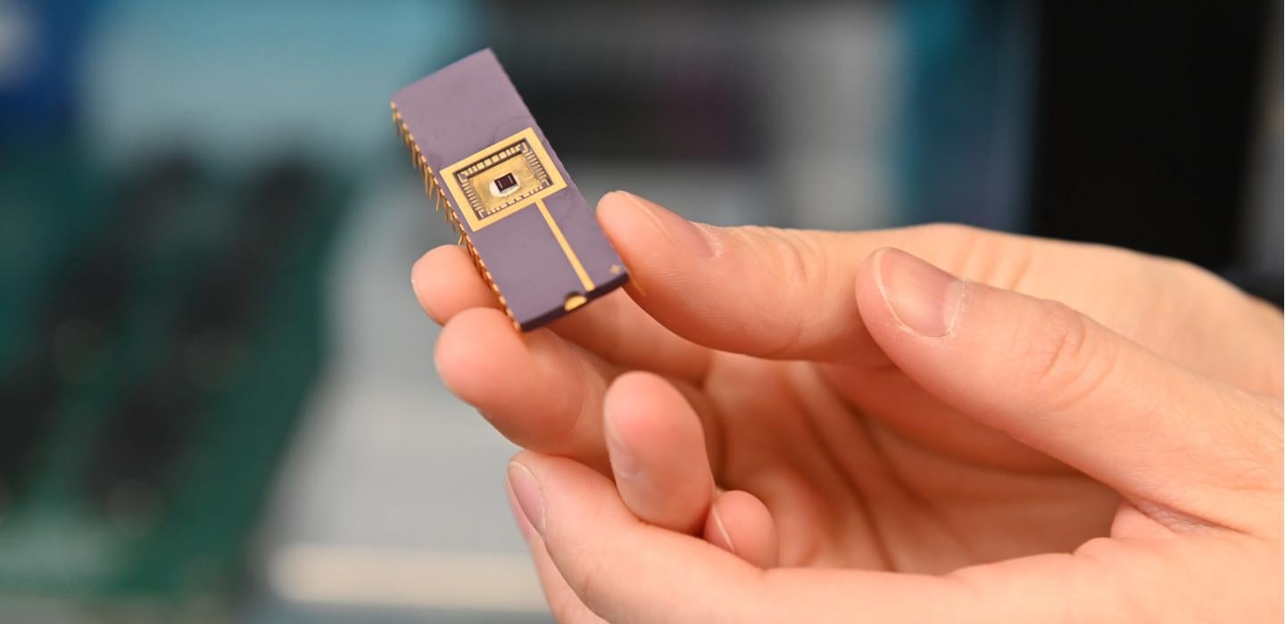 A hand holding a small chip that has gold circuits on the surface