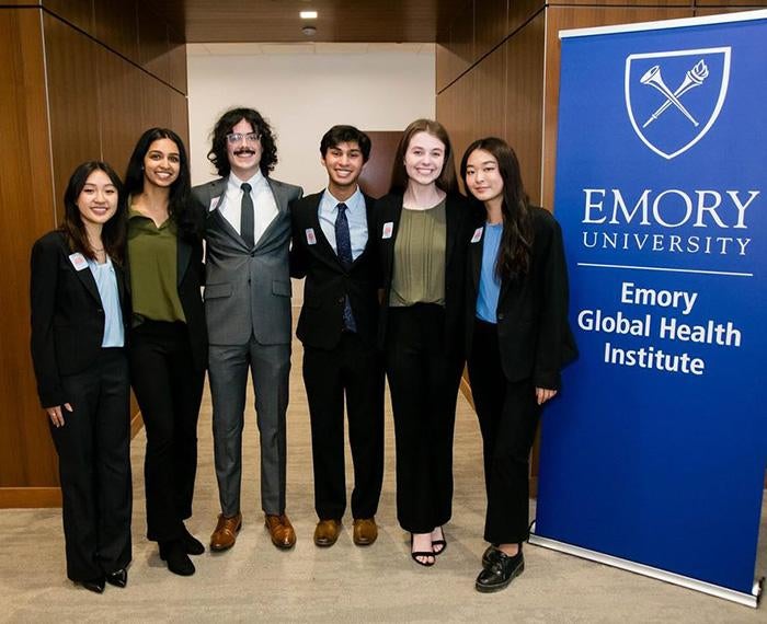 Six students stand beside an Emory University banner
