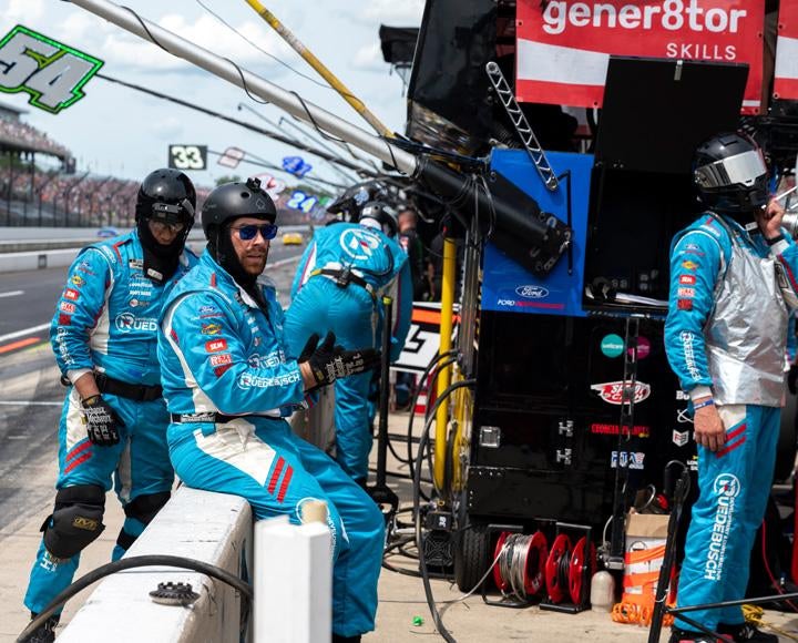 Wilps and other pit crew members watch the race in blue jumpsuits
