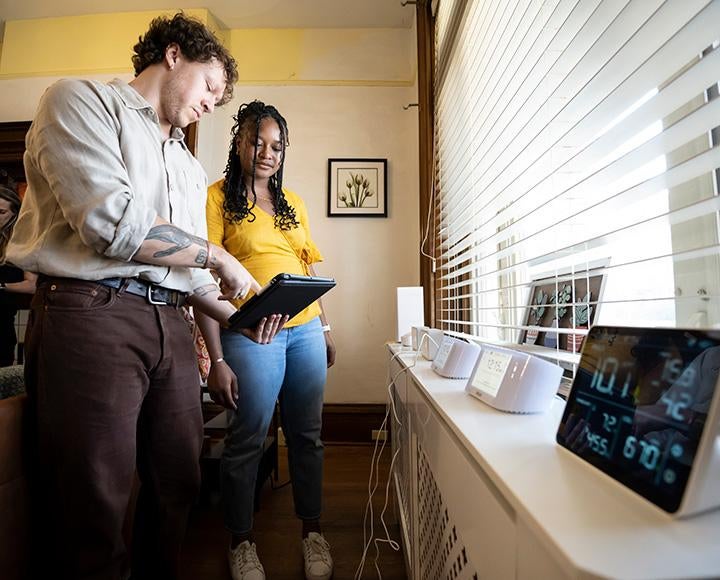 Two researchers look at a tablet. Several smart devices sit on a windowsill