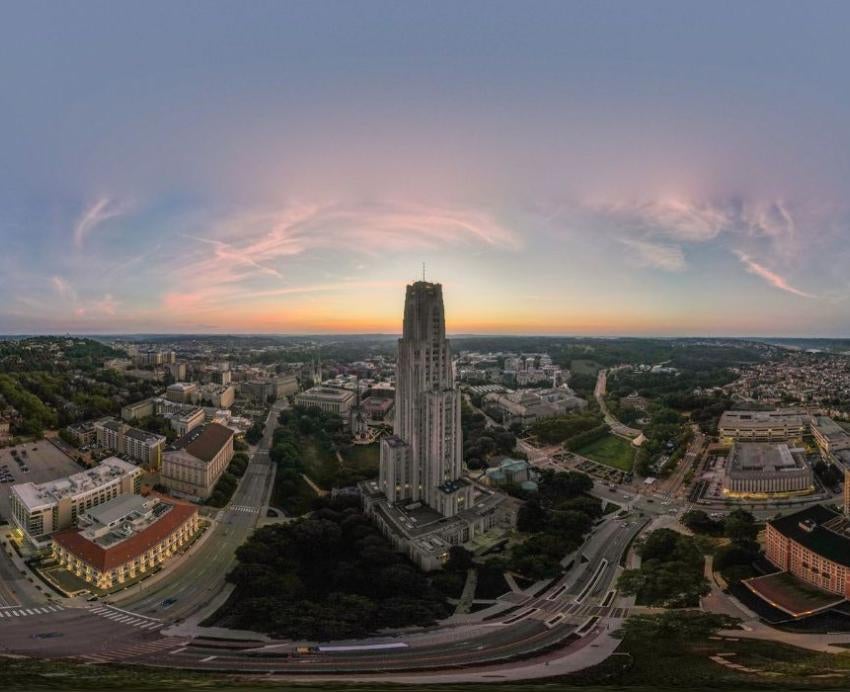 A drone shot shows the sun rising over the Oakland neighborhood and University of Pittsburgh campus, with the Cathedral of Learning in the center.