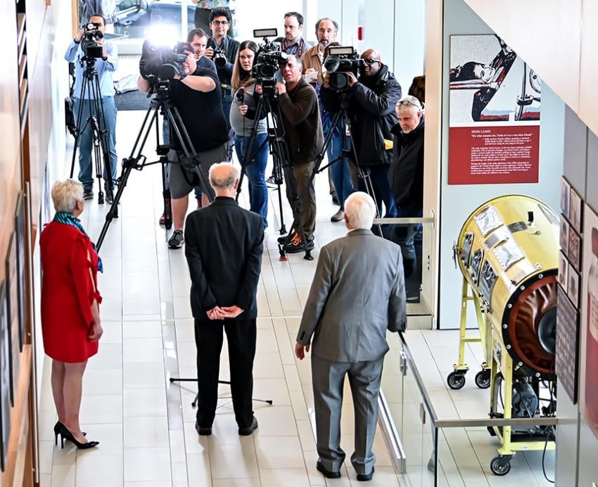 Reporters and cameras stand at the entrance of an exhibit