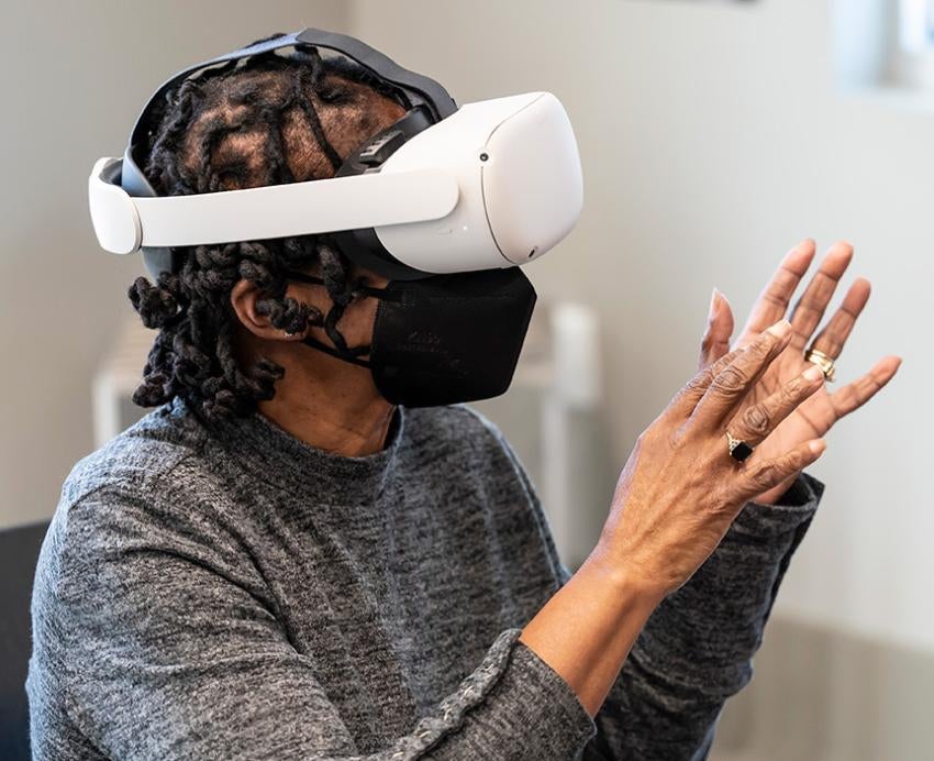 A person wearing a VR headset holds up their hands and speaks to an instructor