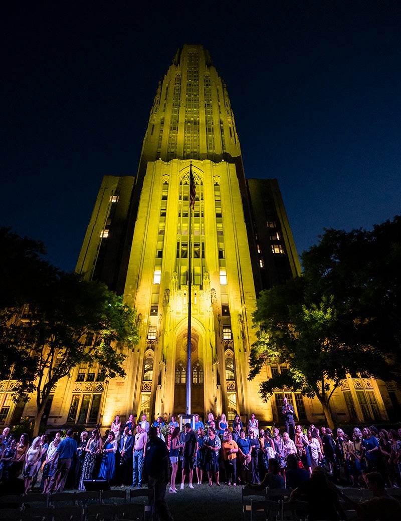 A crowd of people under the Cathedral of Learning at night