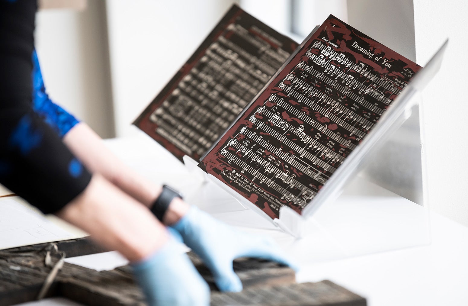 Gloves hands handle printing blocks for sheet music, which is displayed on a stand