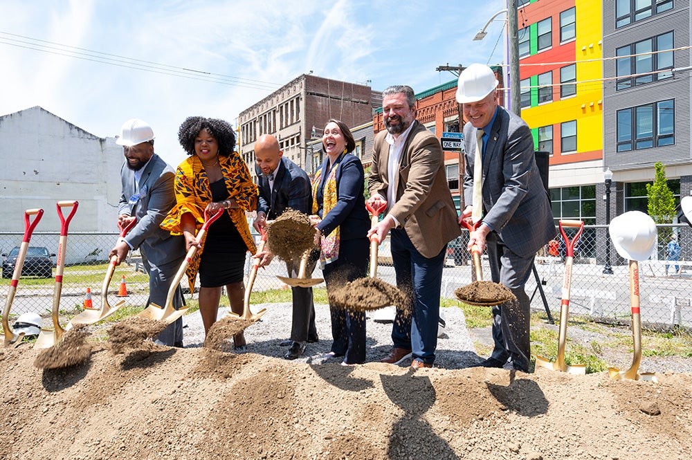 6 people use ceremonial shovels to break ground at a construction site