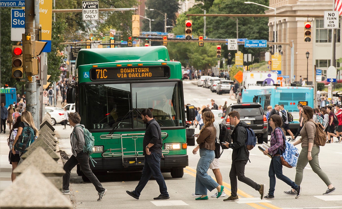 people crossing the street in front of a green bus