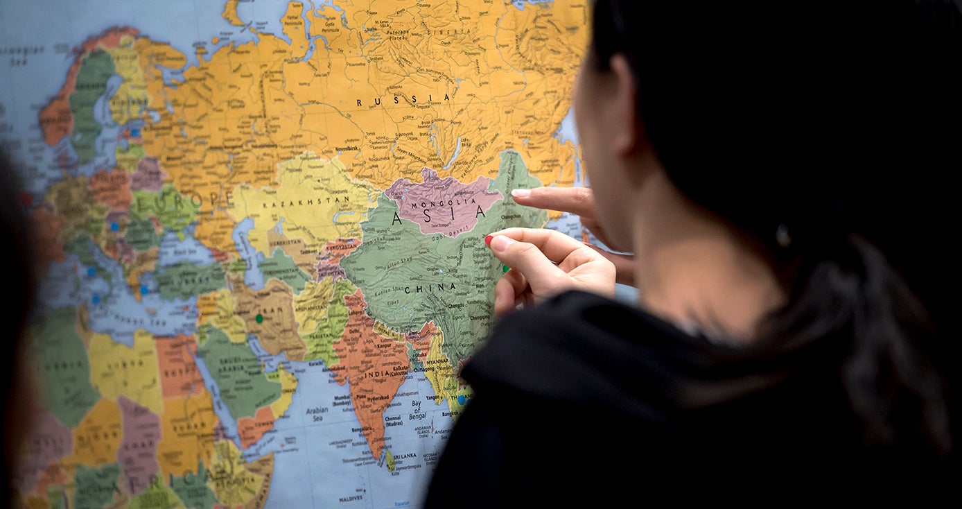 A person in black puts a mark on a map of the world