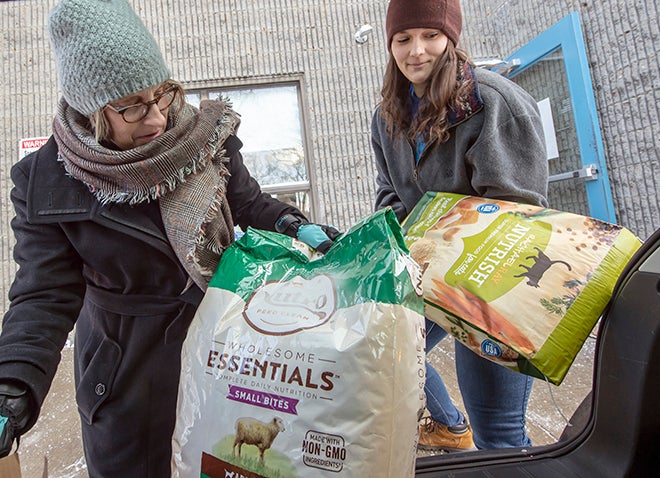 two women unloading bags of pet food from a hatchback trunk