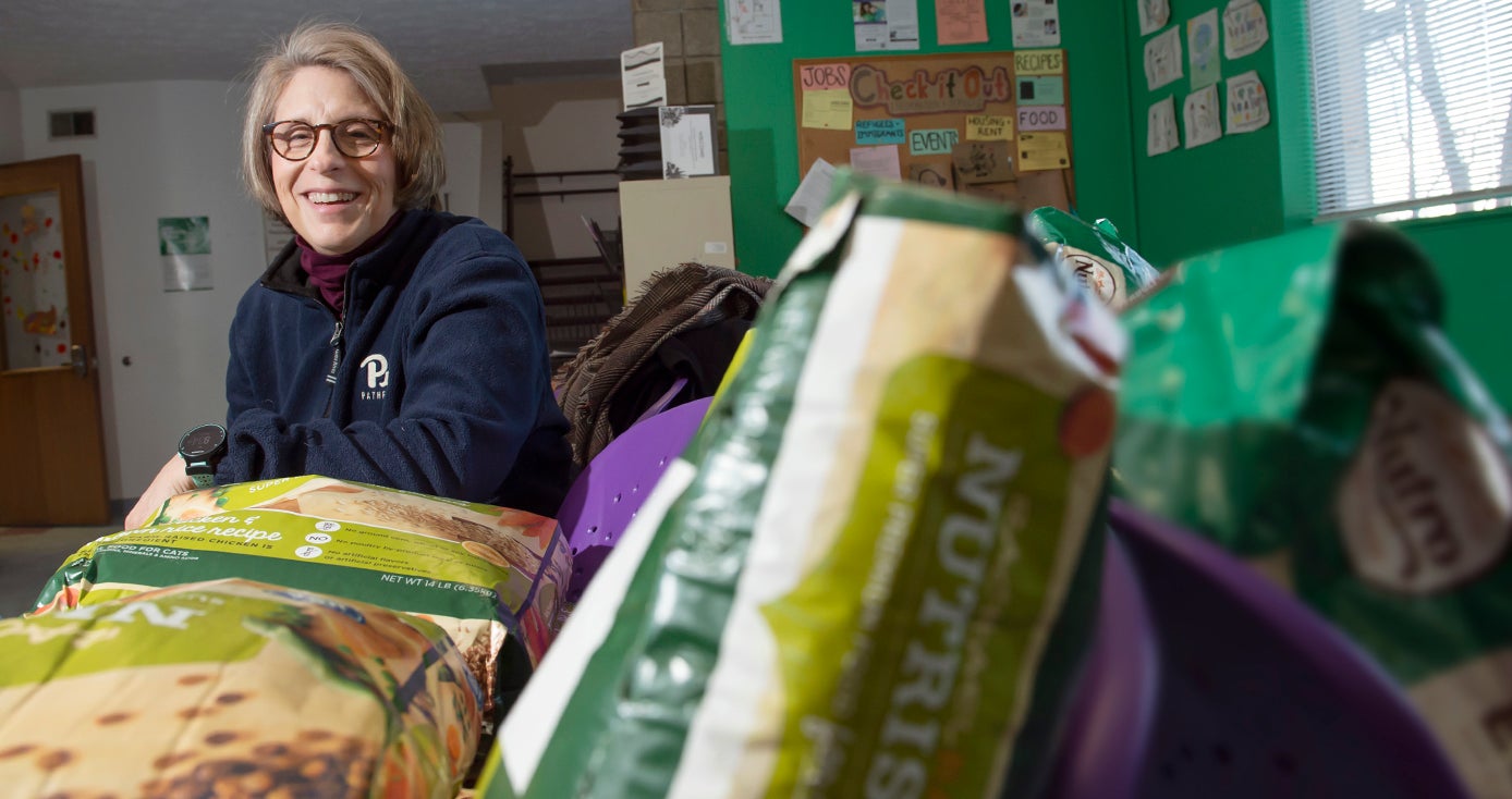 Rauktis, wearing a Pitt fleece, leaning on a table that's piled with big bags of pet food