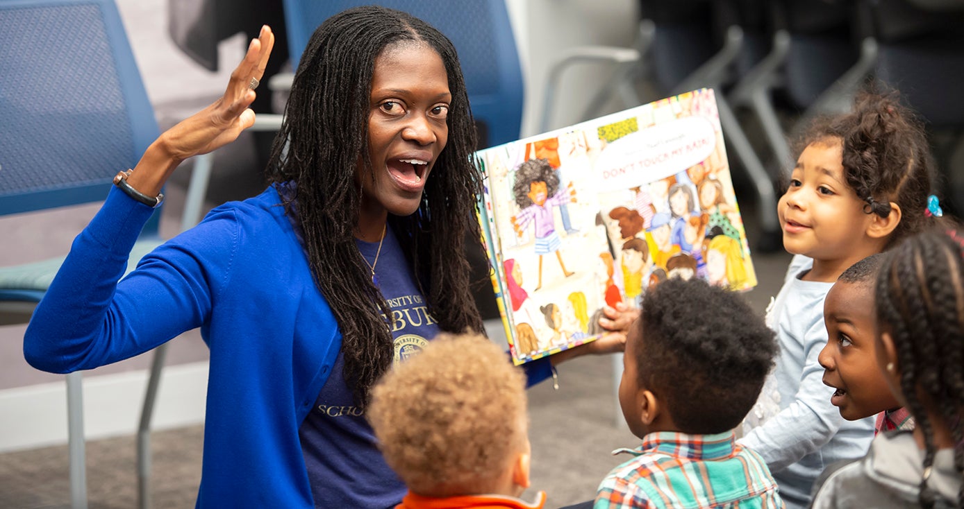 A woman in a blue shirt reading a book to children