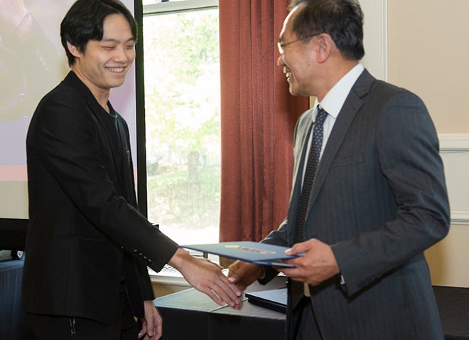a young man in a black suit shaking hands with an administrator