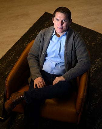 A man in a light blue dress shirt and cardigan sitting in an armchair