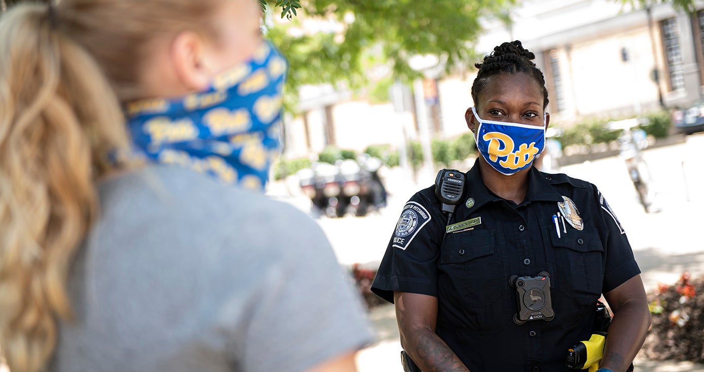 A police officer in a Pitt face mask standing next to a person in a gray shirt