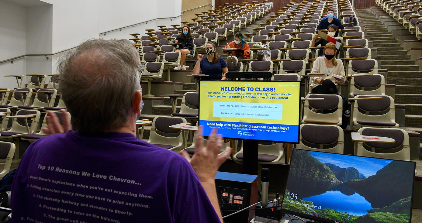 An instructor in a purple shirt teaches a lecture to a mostly empty classroom of masked students