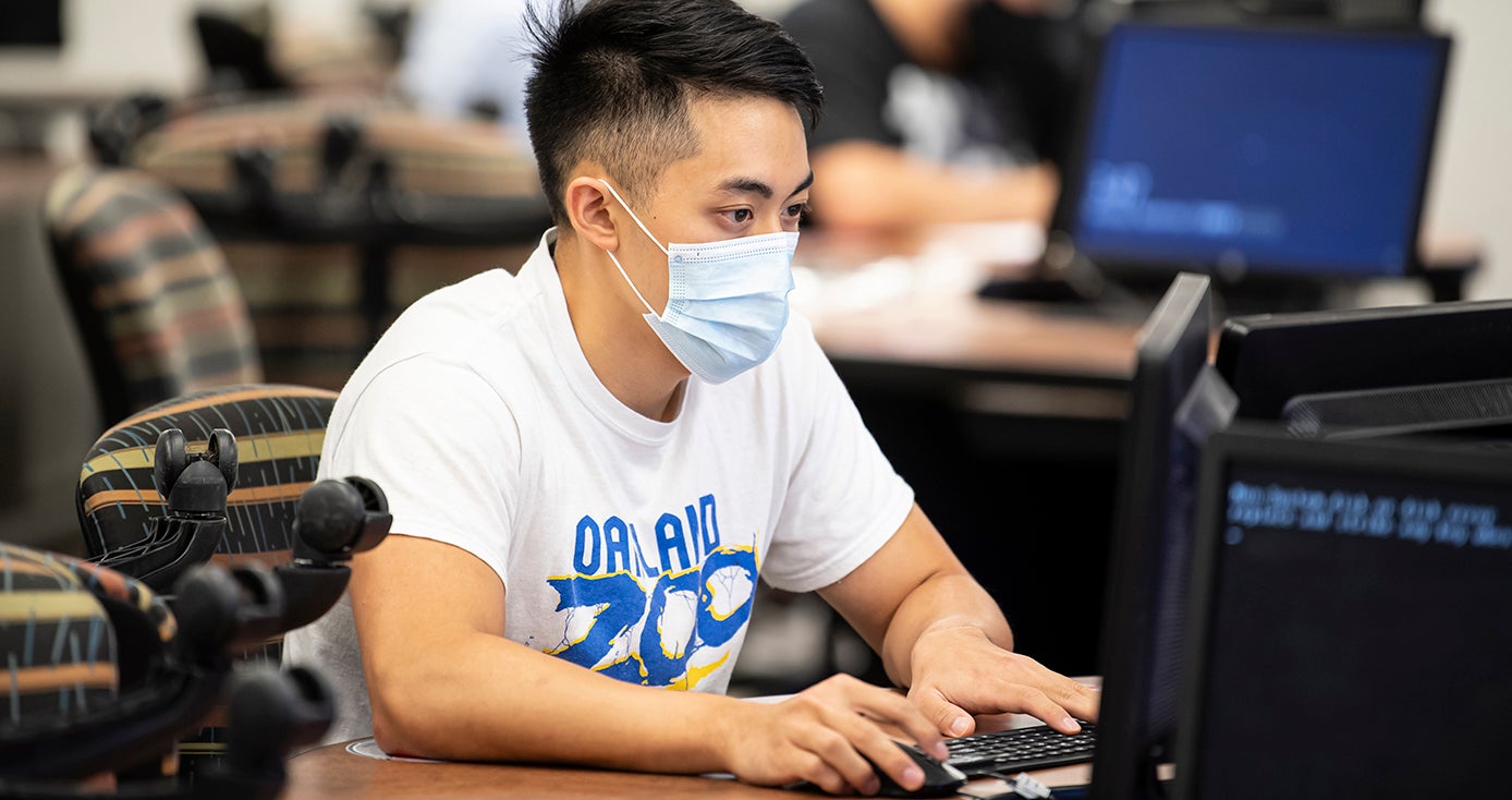 A person in a face mask types on a computer