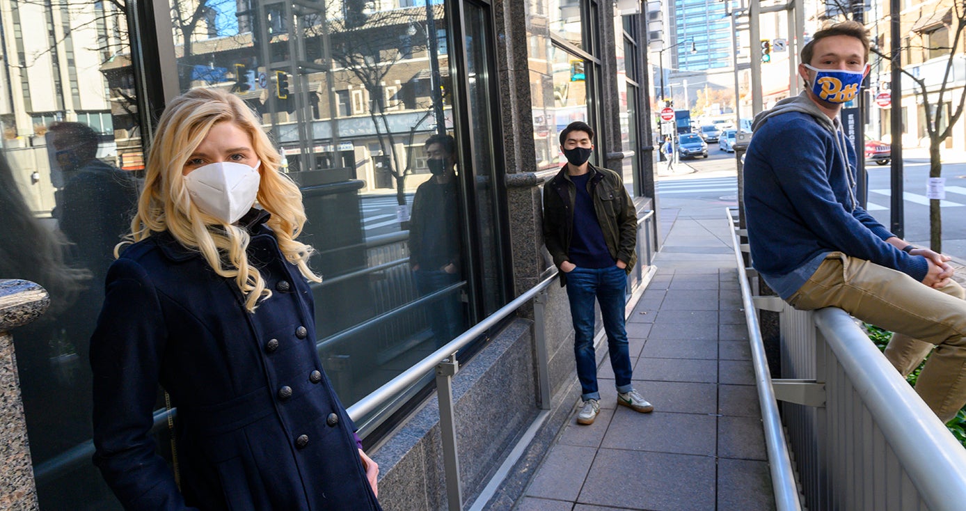 Two people in jackets and face masks on a sidewalk