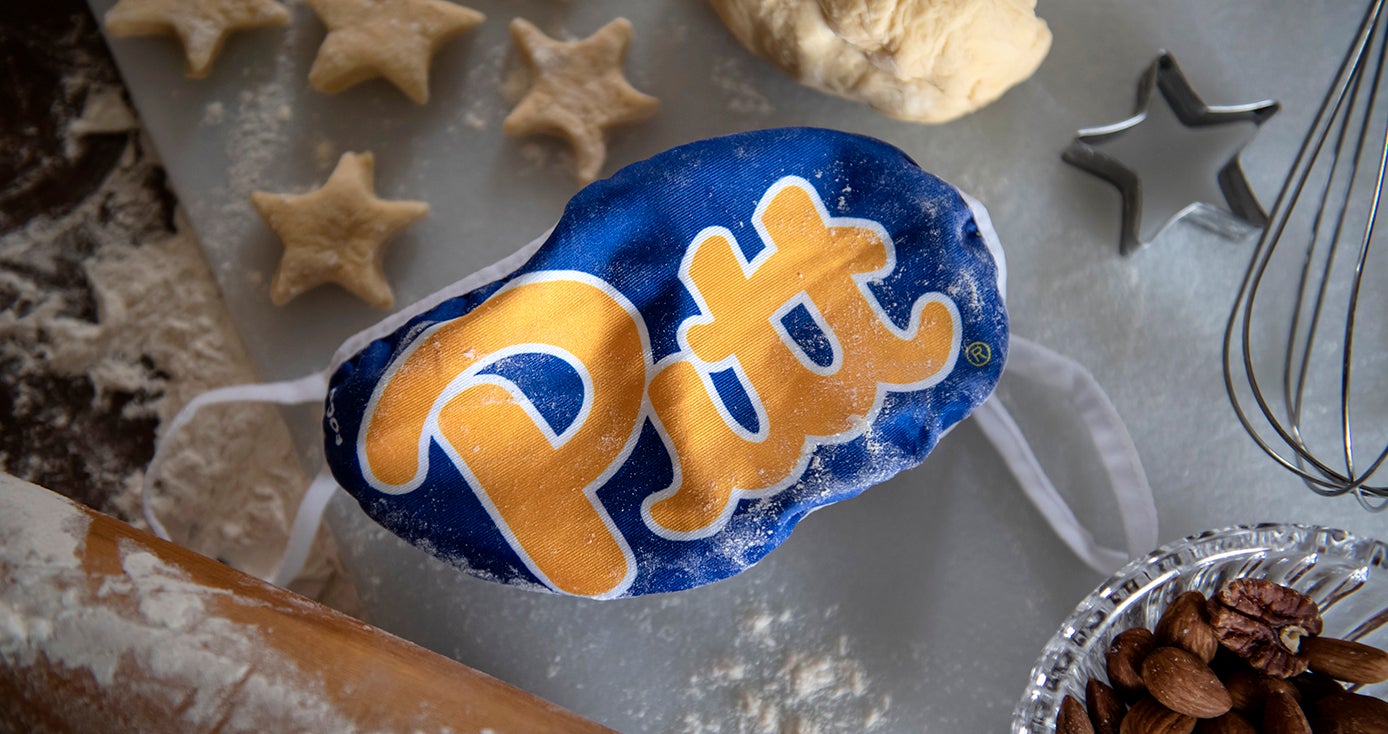 A blue Pitt face mask lying on a table surrounded by cookie dough and cookie cutters