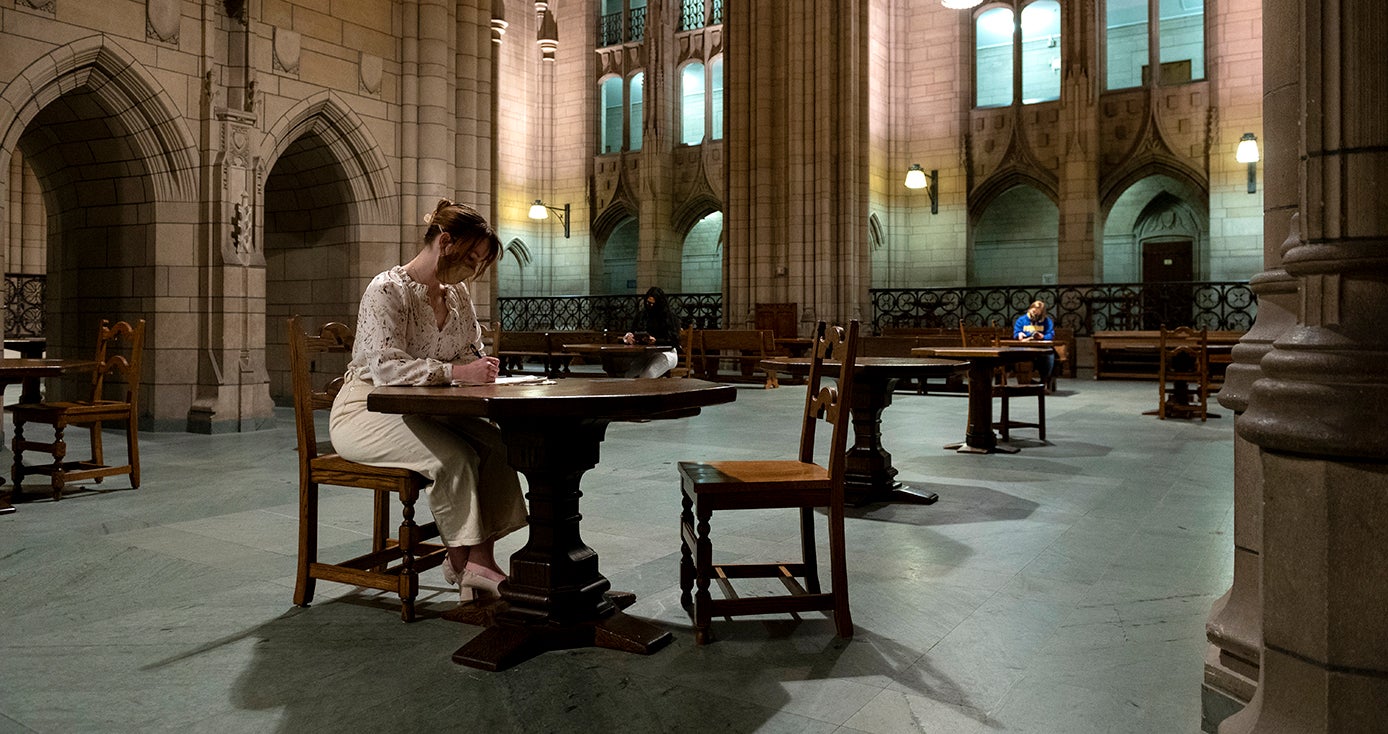 A person in a white outfit studies at a table in the Cathedral of Learning