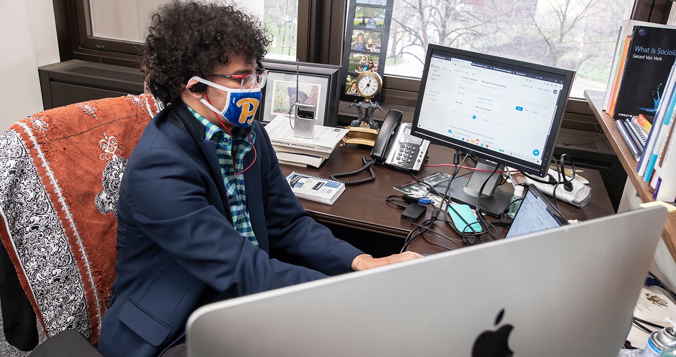 Abdesalam Soudi in a face mask, headphones and a blue jacket, at a computer