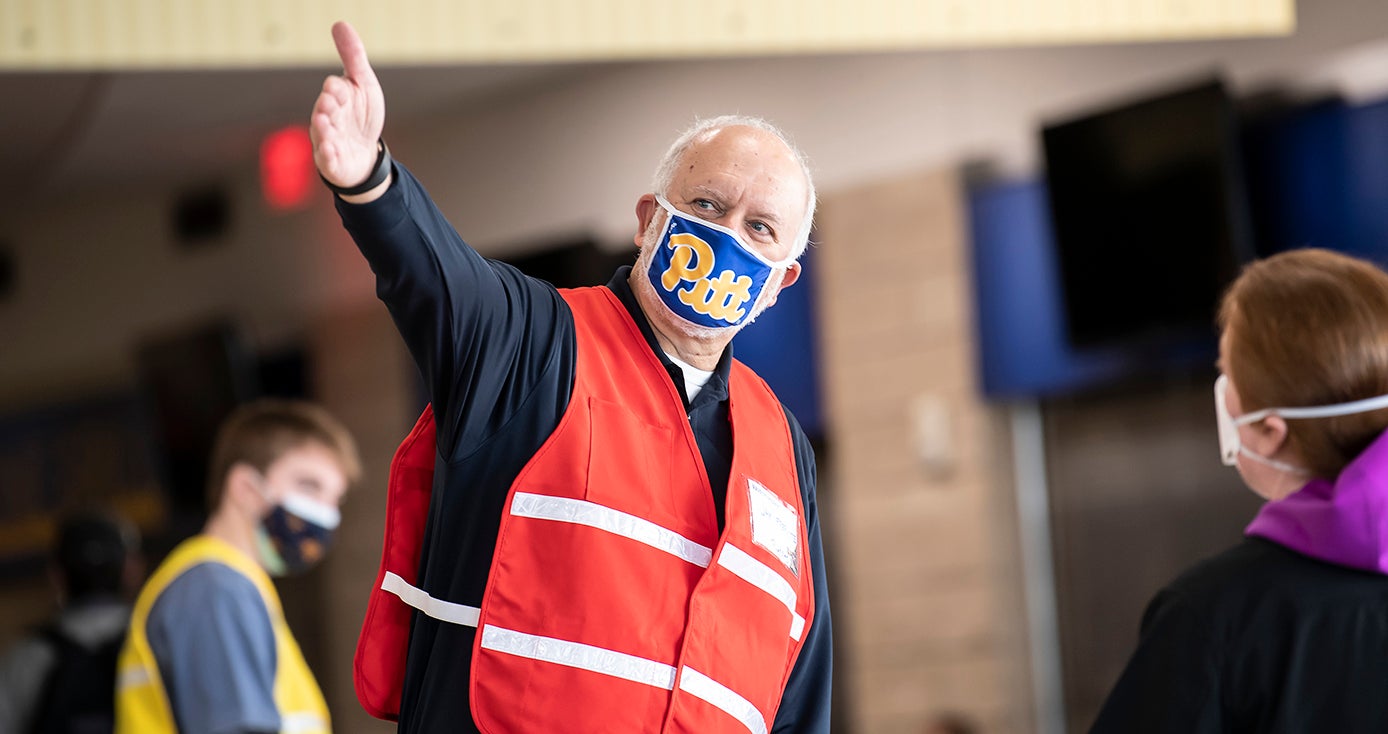 A person in an orange vest and blue face mask points to their right