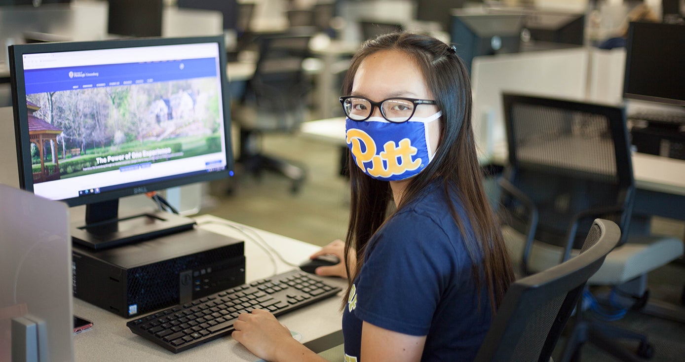 A woman in a blue Pitt face mask and shirt browses the Pitt-Greensburg website