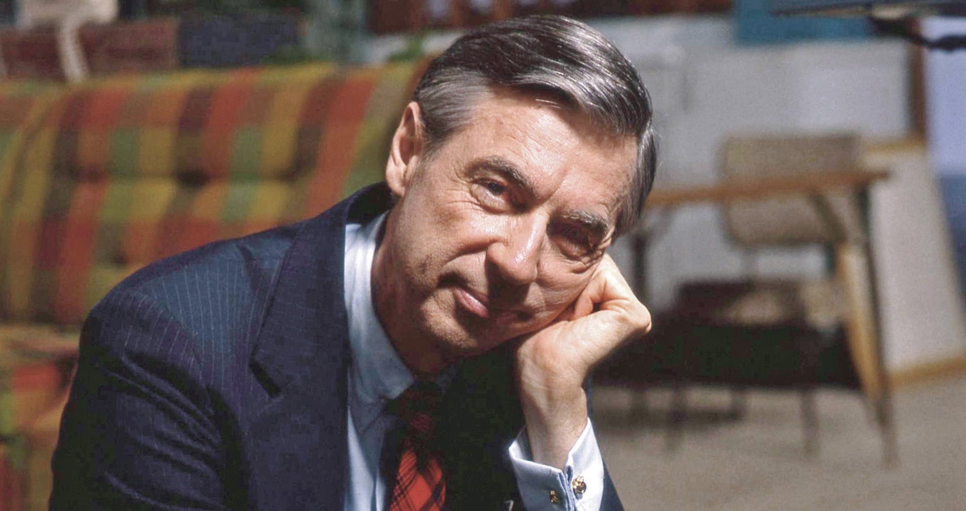 Mr. Rogers in a suit and tie, photographed chest up, resting his head on his fist and looking into camera
