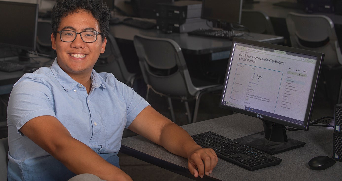 Joseph Valdecanas sitting at a desk in a classroom, showcasing a website that he helped create.