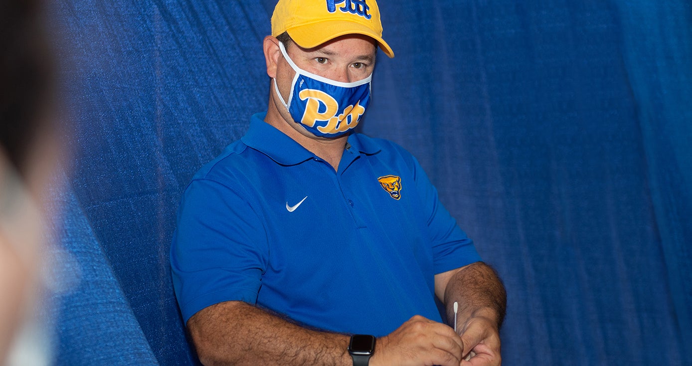 A person in a blue face mask and yellow Pitt hat