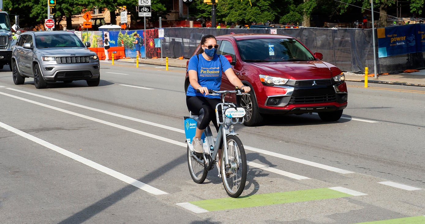 A person in a blue shirt and face mask bicycles on the street
