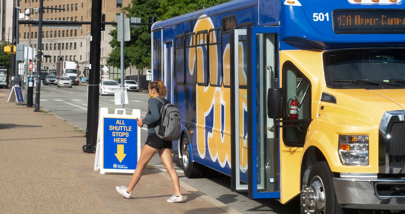 A person with a backpack and face mask disembarks a campus shuttle