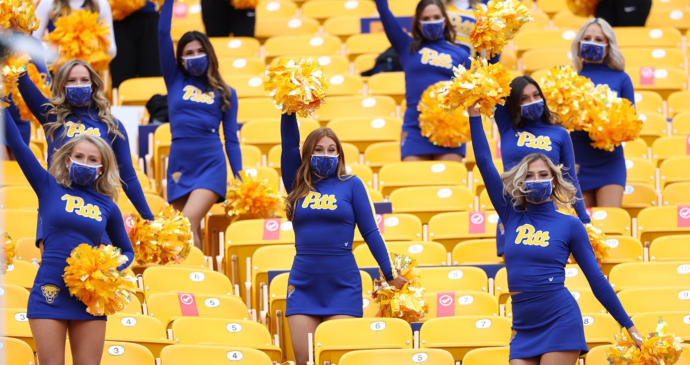 Cheerleaders in face masks hold pom poms in the seats