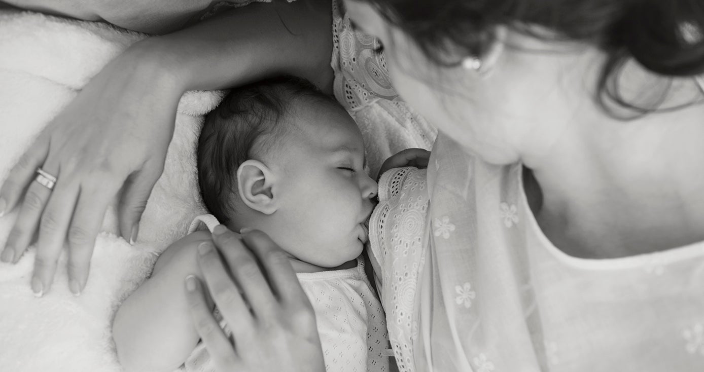 a black and white image of a baby feeding with their mom