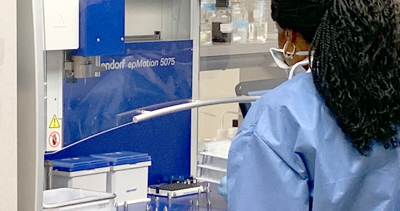 A person with a blue gown and face mask stands by a machine