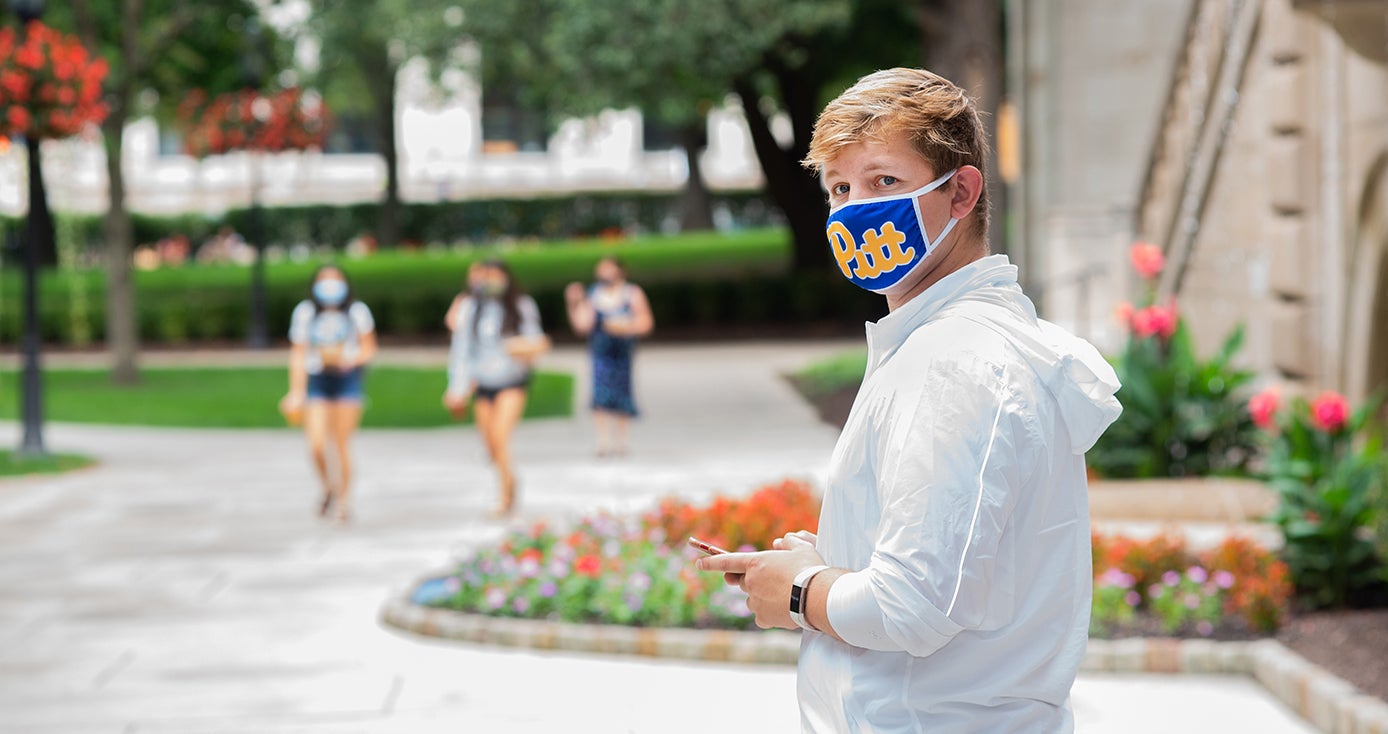 A person in a Pitt face mask holding a phone