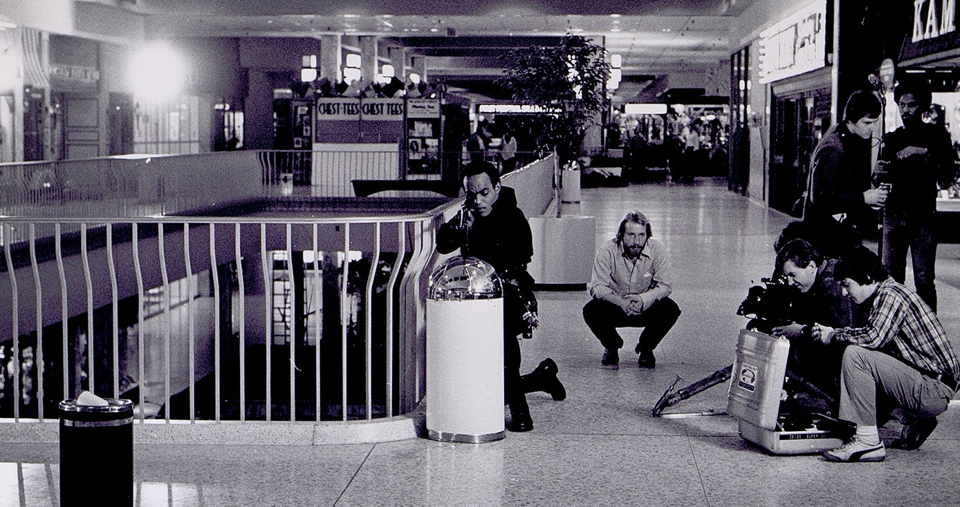 a black and white photo of a camera crew shooting a scene in a mall