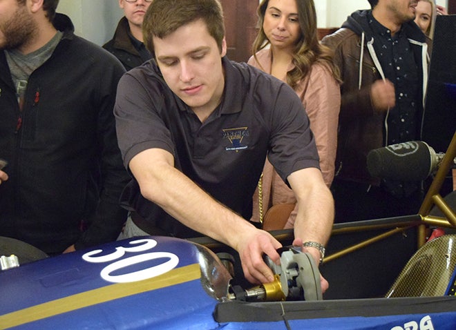 male student working on racecar with a few onlookers in background