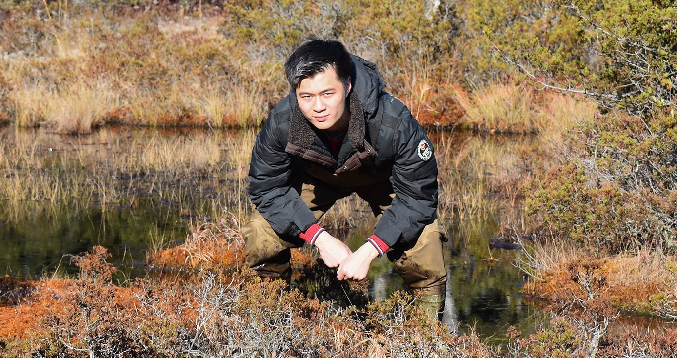 Alvin Liu crouching near a body of water, next to shrubbery