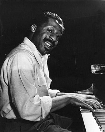 Black and white historical photo of jazz musician Erroll Garner playing the piano.