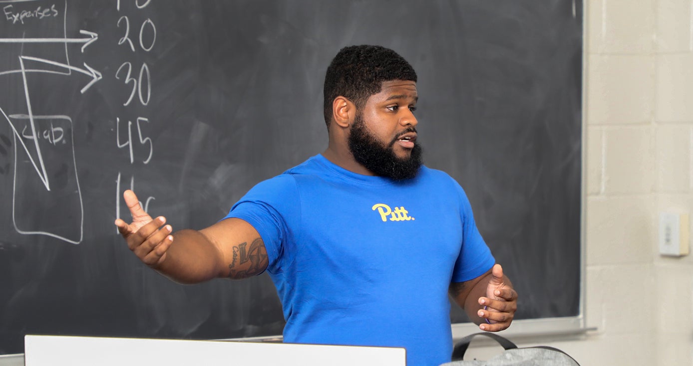 Christopher Darby in front of a blackboard, wearing a blue Pitt shirt