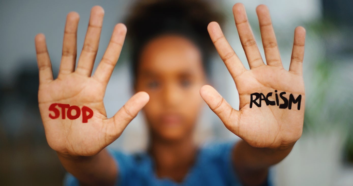 A person in a blue shirt holds up their hands with the words "Stop Racism" written on them. 
