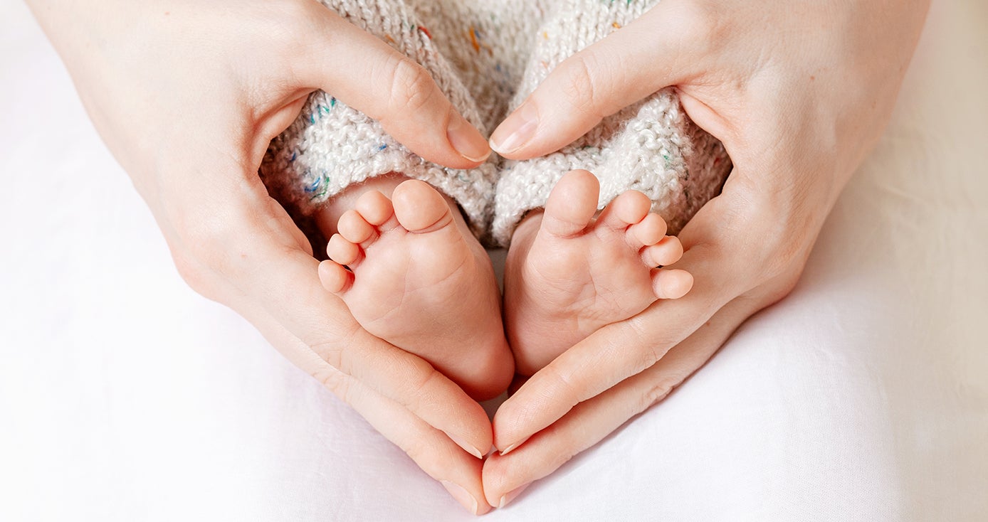 A person making a heart with their hands around a baby's feet