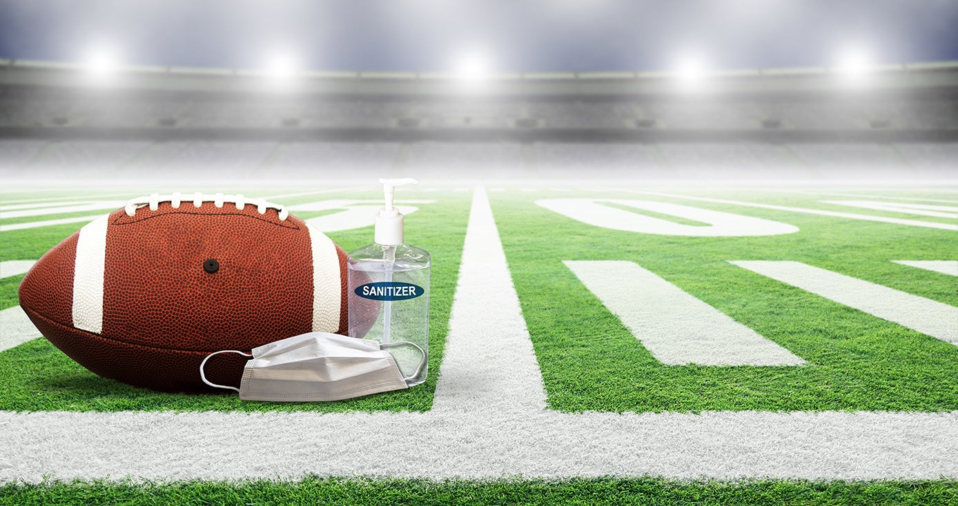 A football, a face mask and a bottle of hand sanitizer on a football field