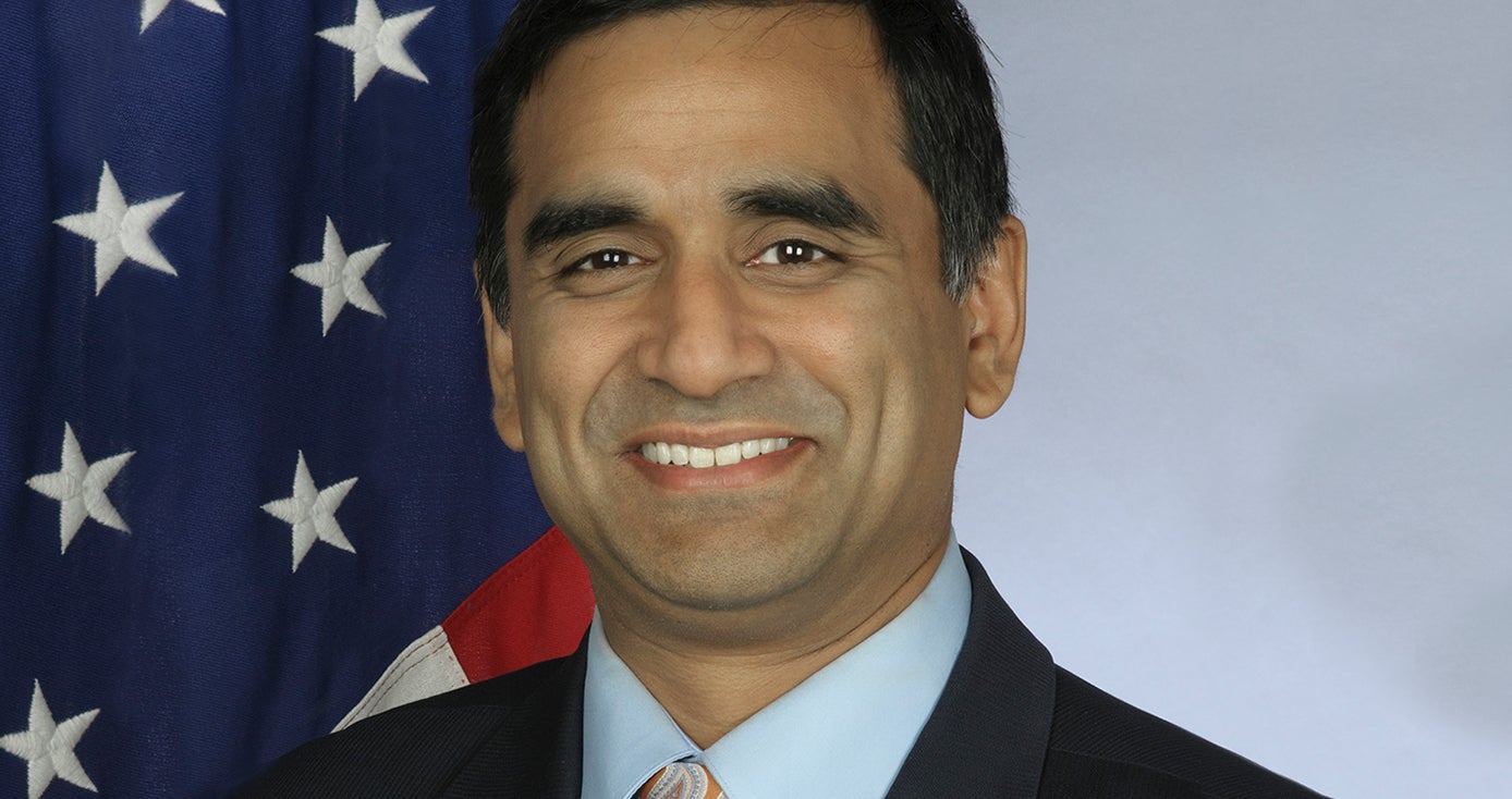 Hari Sastry headshot, in suit jacket, shirt and tie in front of American flag