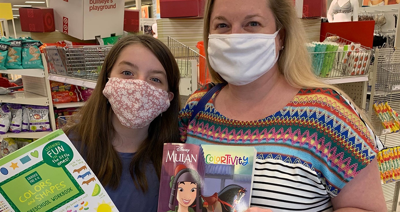 Two people in face masks hold up books while in a store