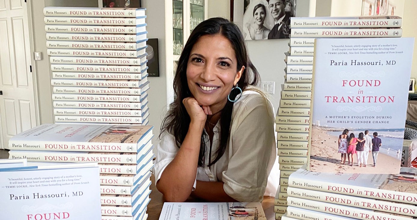 Paria Hassouri in a white top leaning on her elbows on a table with stacks of books