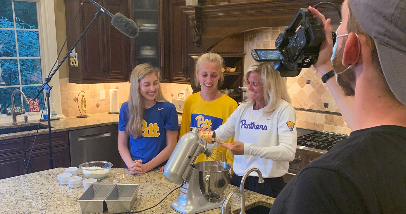 Heather Lyke with two children in Pitt shirts bake in a kitchen together while a camera crew films