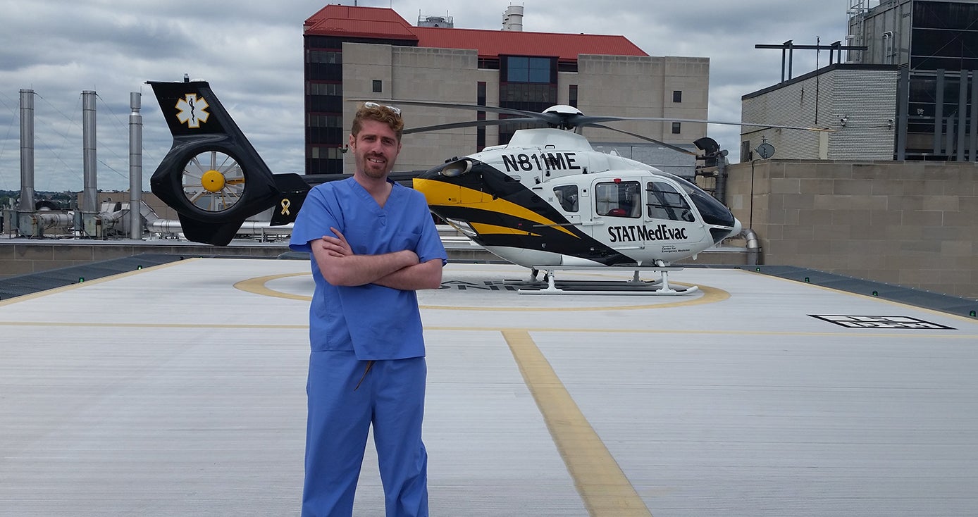 A man in blue scrubs standing by a helicopter