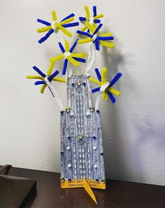 A colored cutout of the Cathedral of Learning with blue and yellow fireworks attached