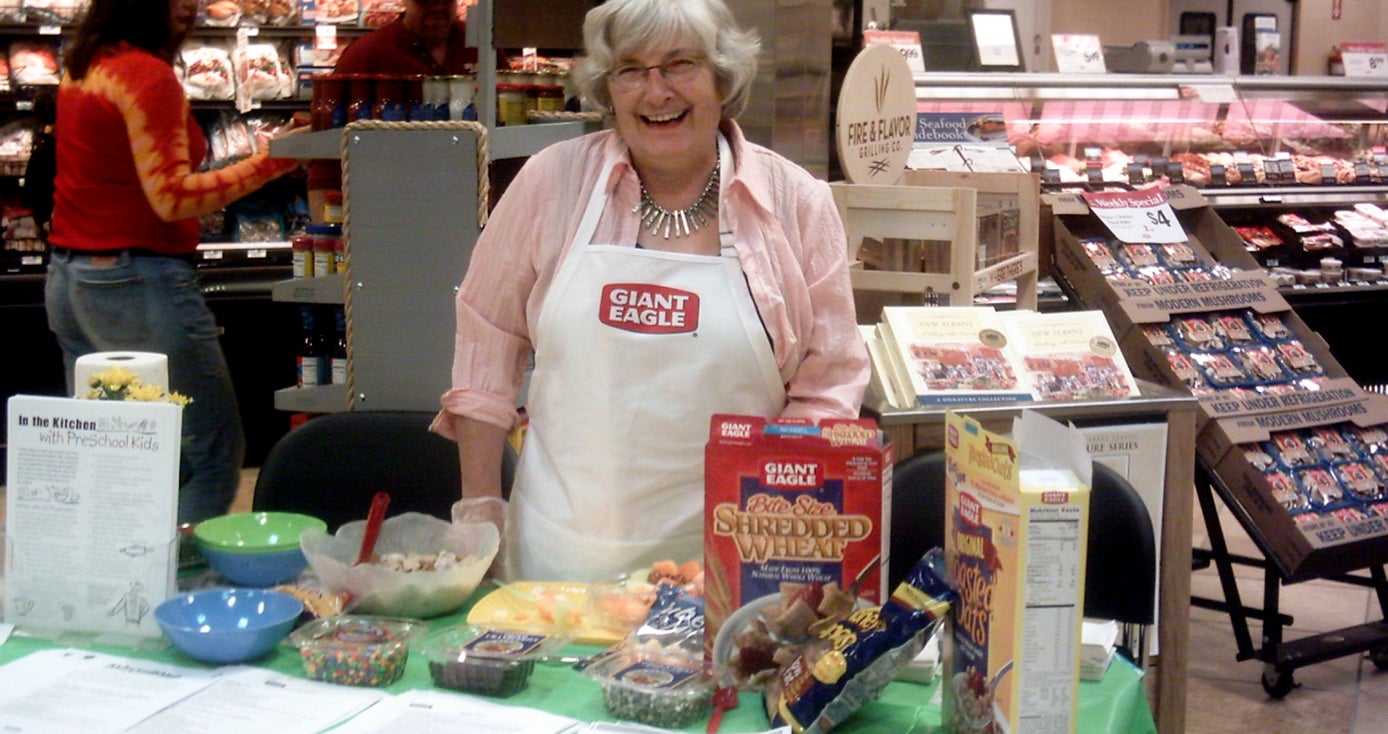 a woman in a Giant Eagle white apron standing behind a table displaying various cereals